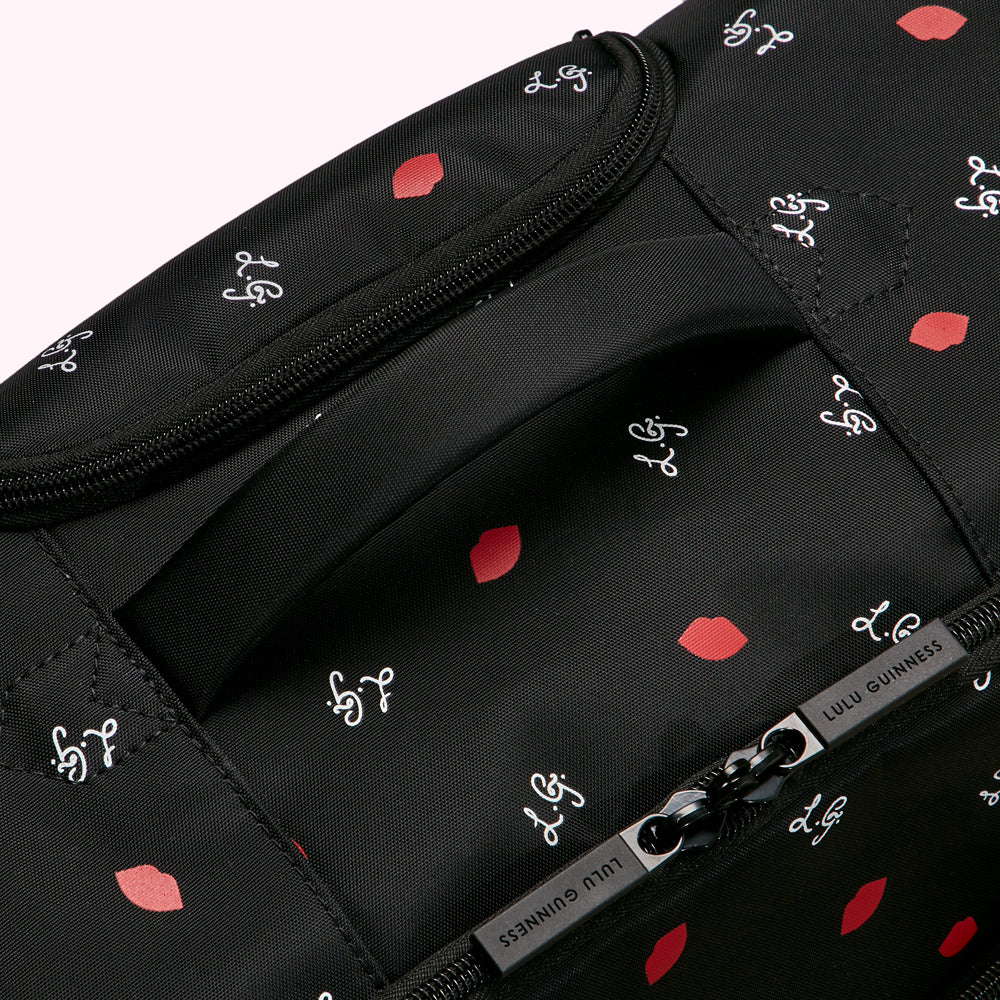 Close-up of a black Lulu Guinness bag with a red lips and cursive logo print, showing the top handle and zipper.
