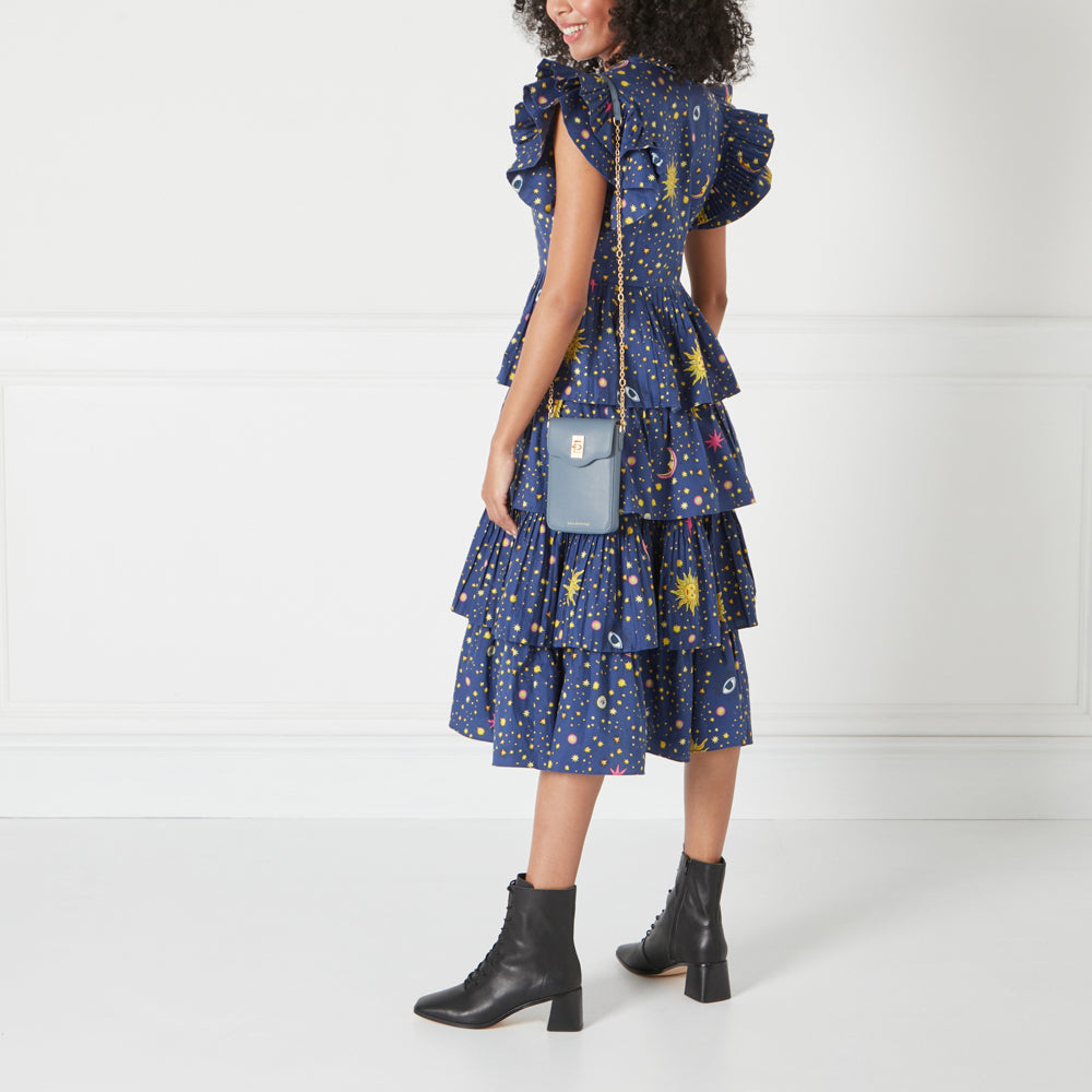 Woman in a blue dress with celestial print and black ankle boots carrying a small blue crossbody bag.
