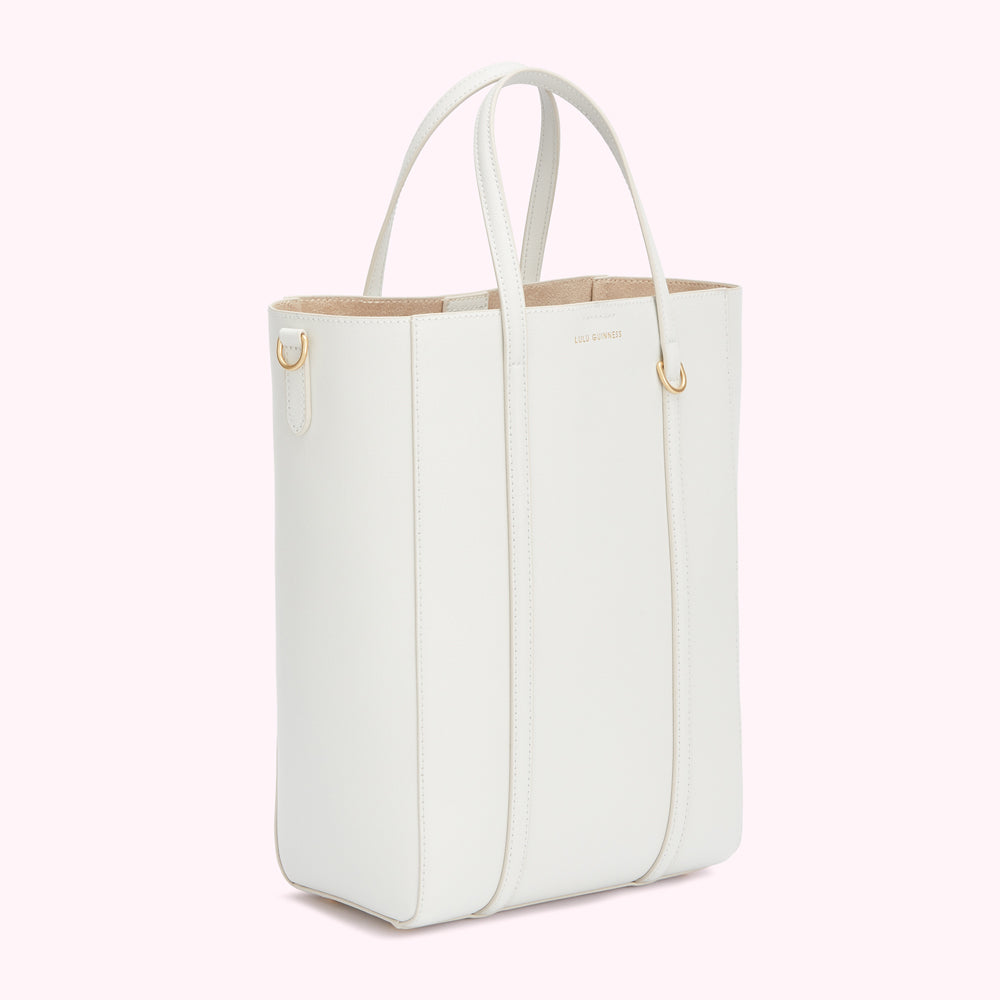 Off-white Lulu Guinness tote bag with gold-toned hardware against a light pink background.
