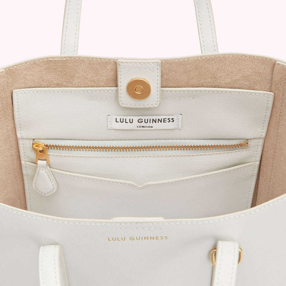 Inside of a cream-colored Lulu Guinness tote bag, showing the interior pocket and brand label.

