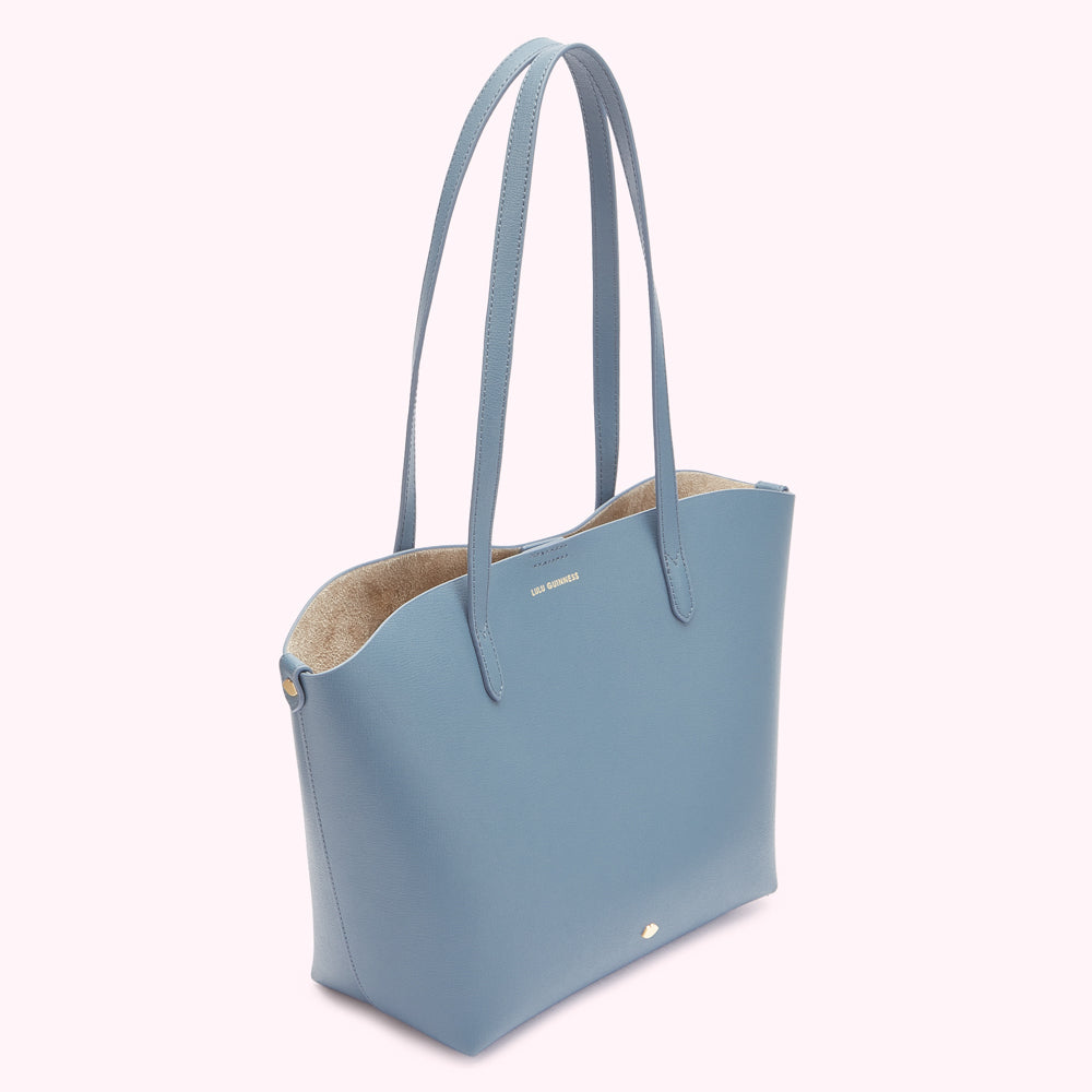 A light blue tote bag with tan interior and gold logo.