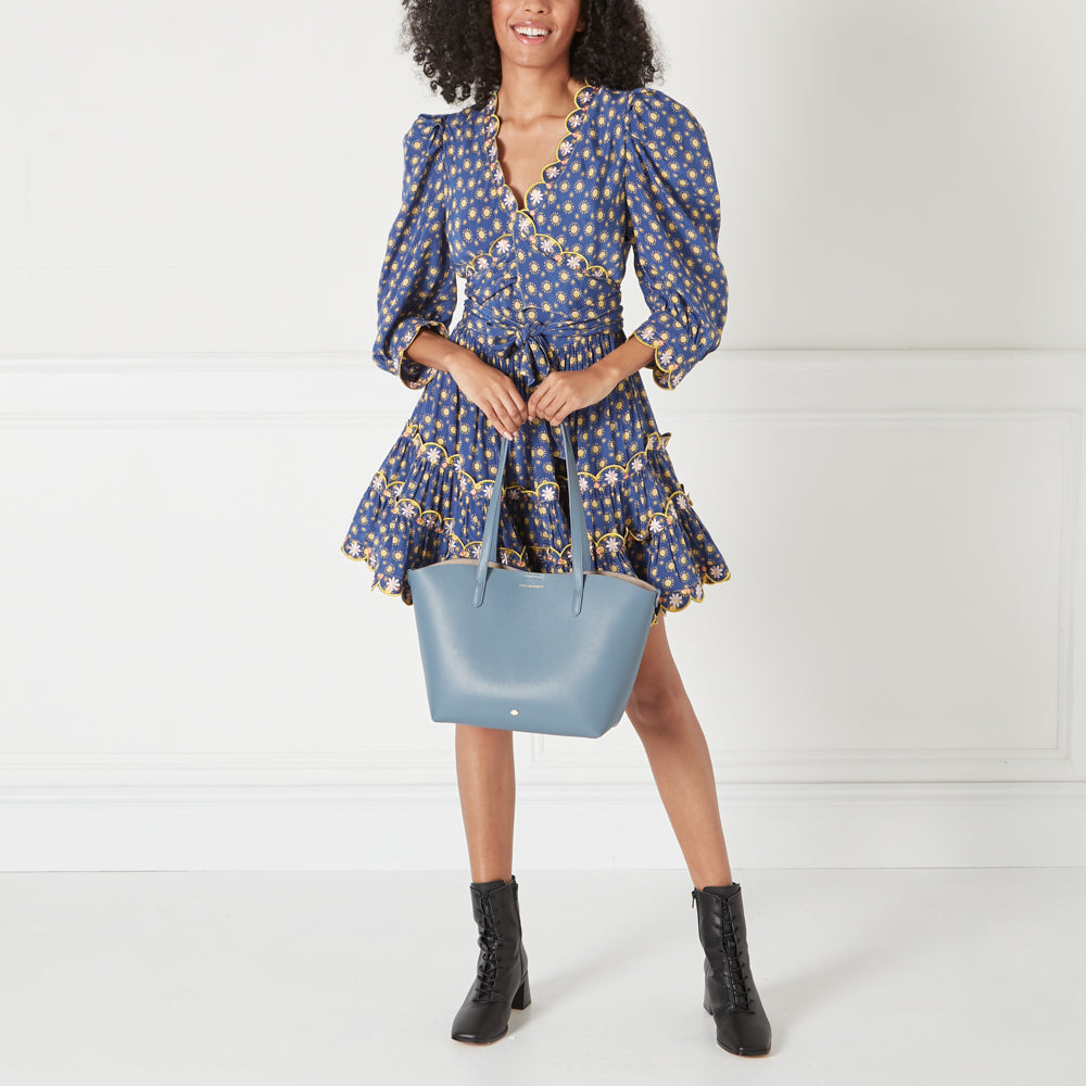 Woman in blue floral dress holding a blue tote bag.
