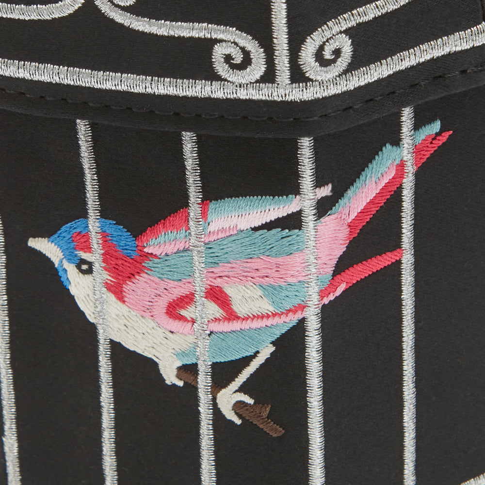 Close-up of embroidered bird in cage on black fabric with silver accents.
