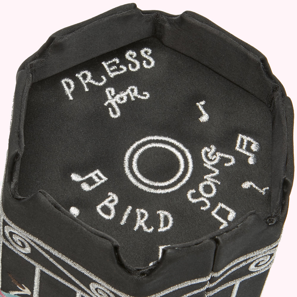 Close-up of a black fabric item with embroidered text "PRESS for BIRD Song" and musical notes.