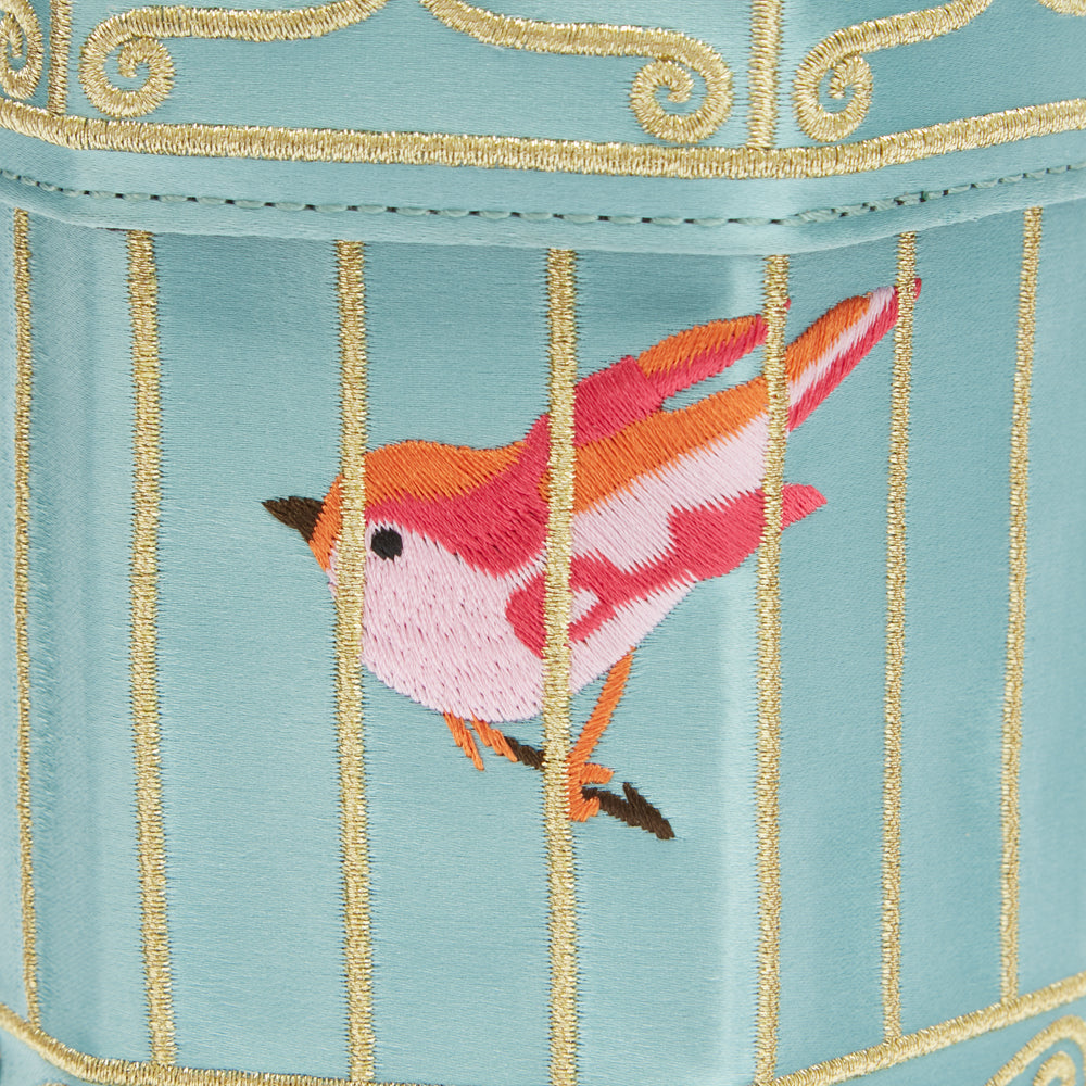 Close-up of embroidered bird in cage on light blue fabric.