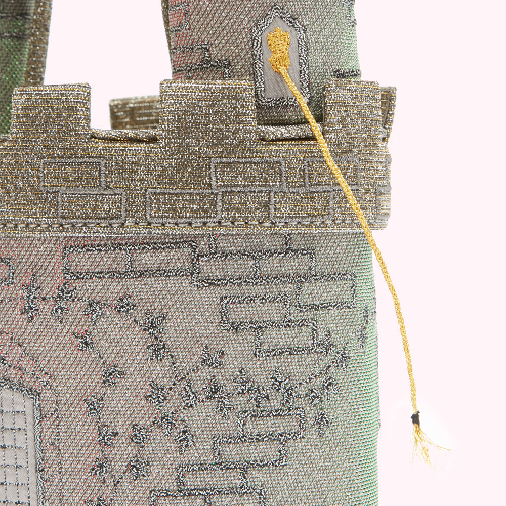 Close-up of a silver and gold castle-shaped handbag with a gold strand of Rapunzel's hair.