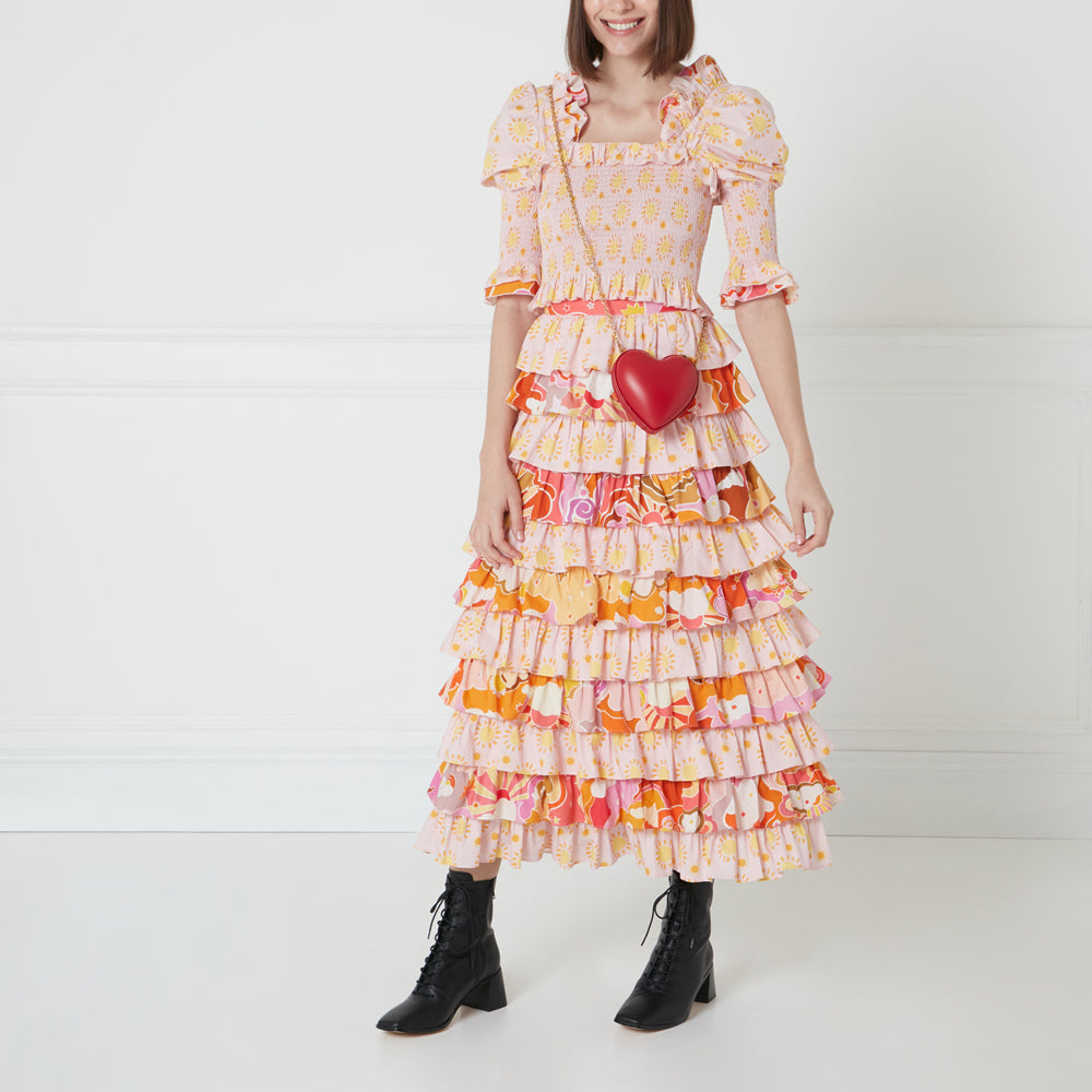 Woman in a pink and orange tiered midi dress and black lace-up boots, carrying a red heart-shaped handbag.
