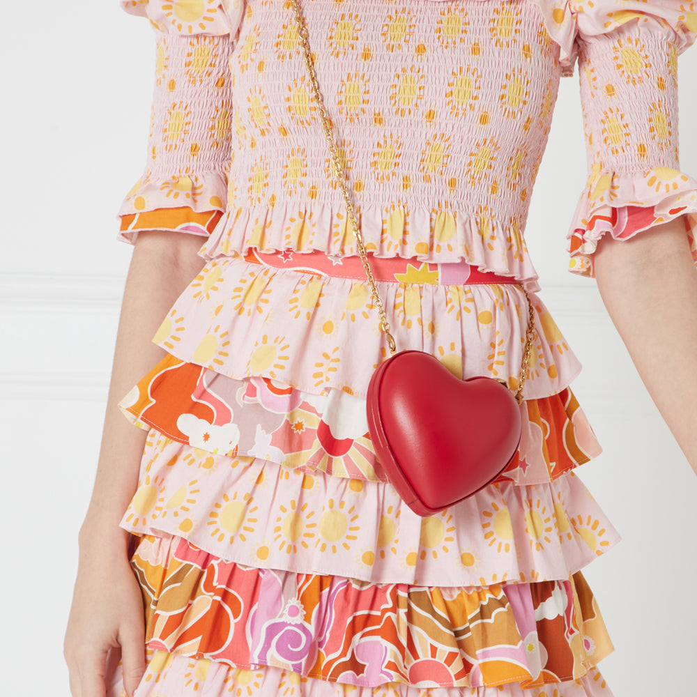 Close-up of a red heart-shaped purse worn over a pink and orange tiered dress with a sun pattern.