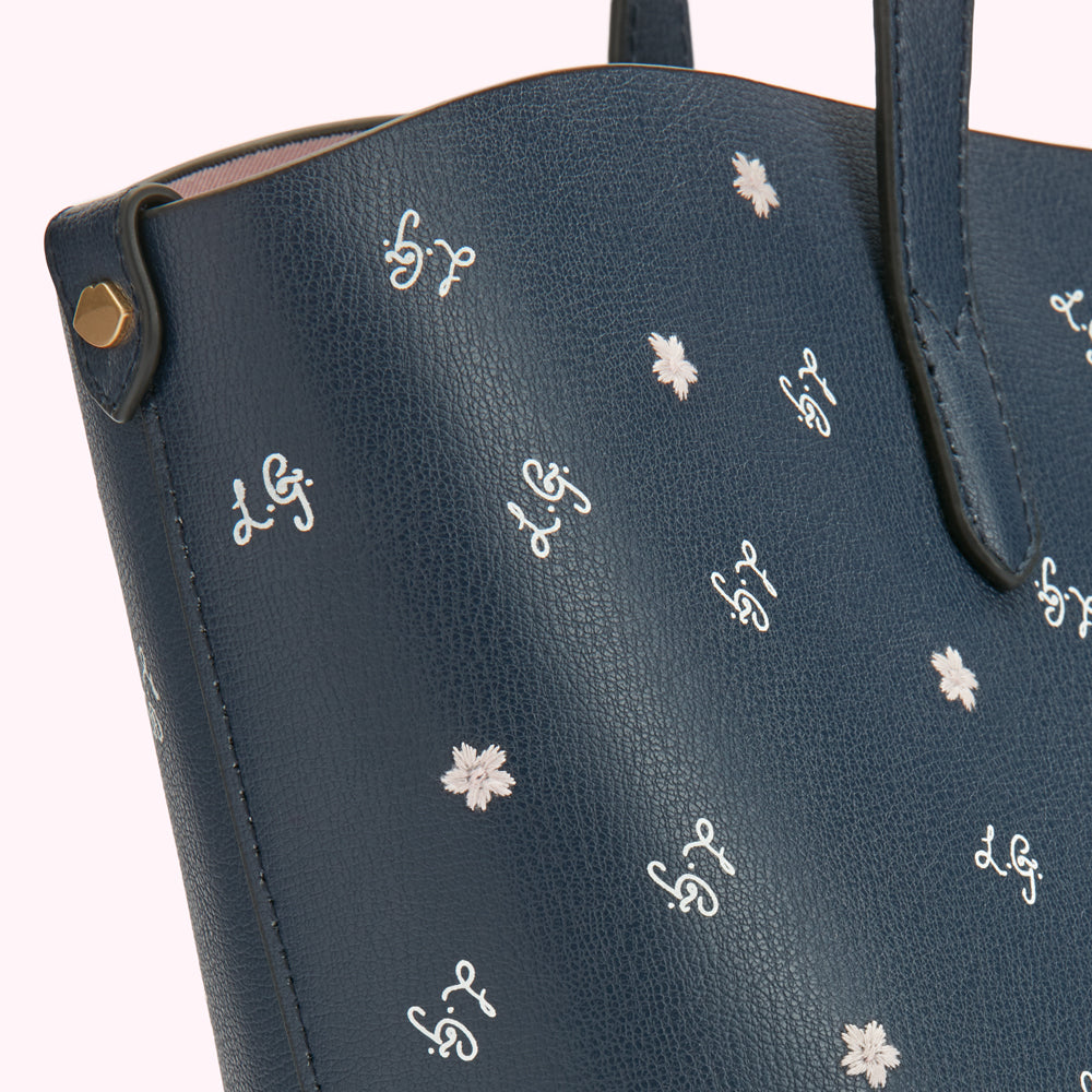 Close-up of a navy blue tote bag with a repeating pattern of small flowers and the initials "L.G." embroidered in off-white.