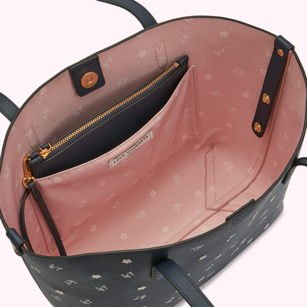 Inside of a navy blue Lulu Guinness tote bag with a pink interior featuring a repeating logo pattern; a smaller navy blue zippered pocket is visible.
