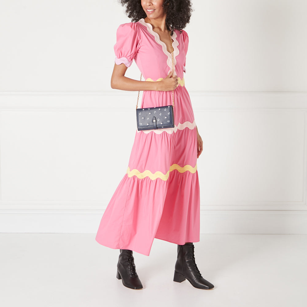 Woman in pink dress holding a navy blue floral crossbody wallet on a gold chain.
