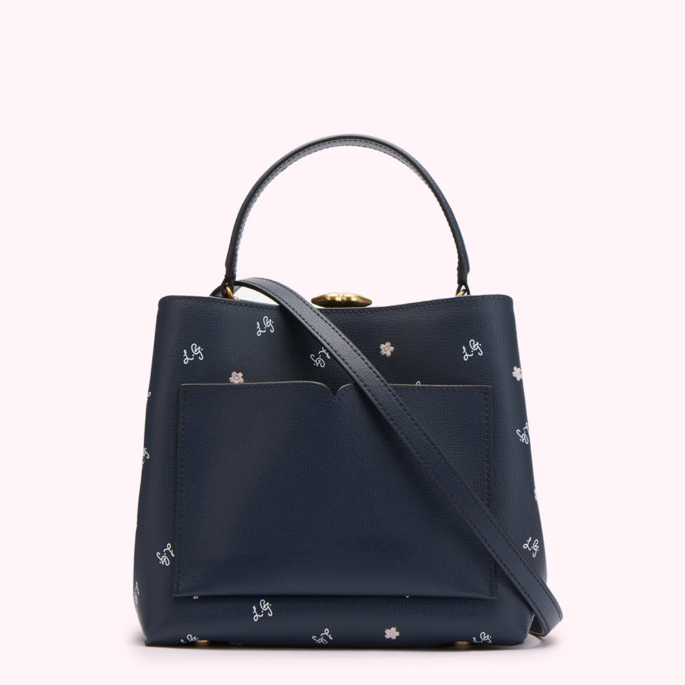 Navy blue leather handbag with a small front pocket, top handles, and a crossbody strap; the bag is decorated with a repeating pattern of small white flowers and the initials "L.G."
