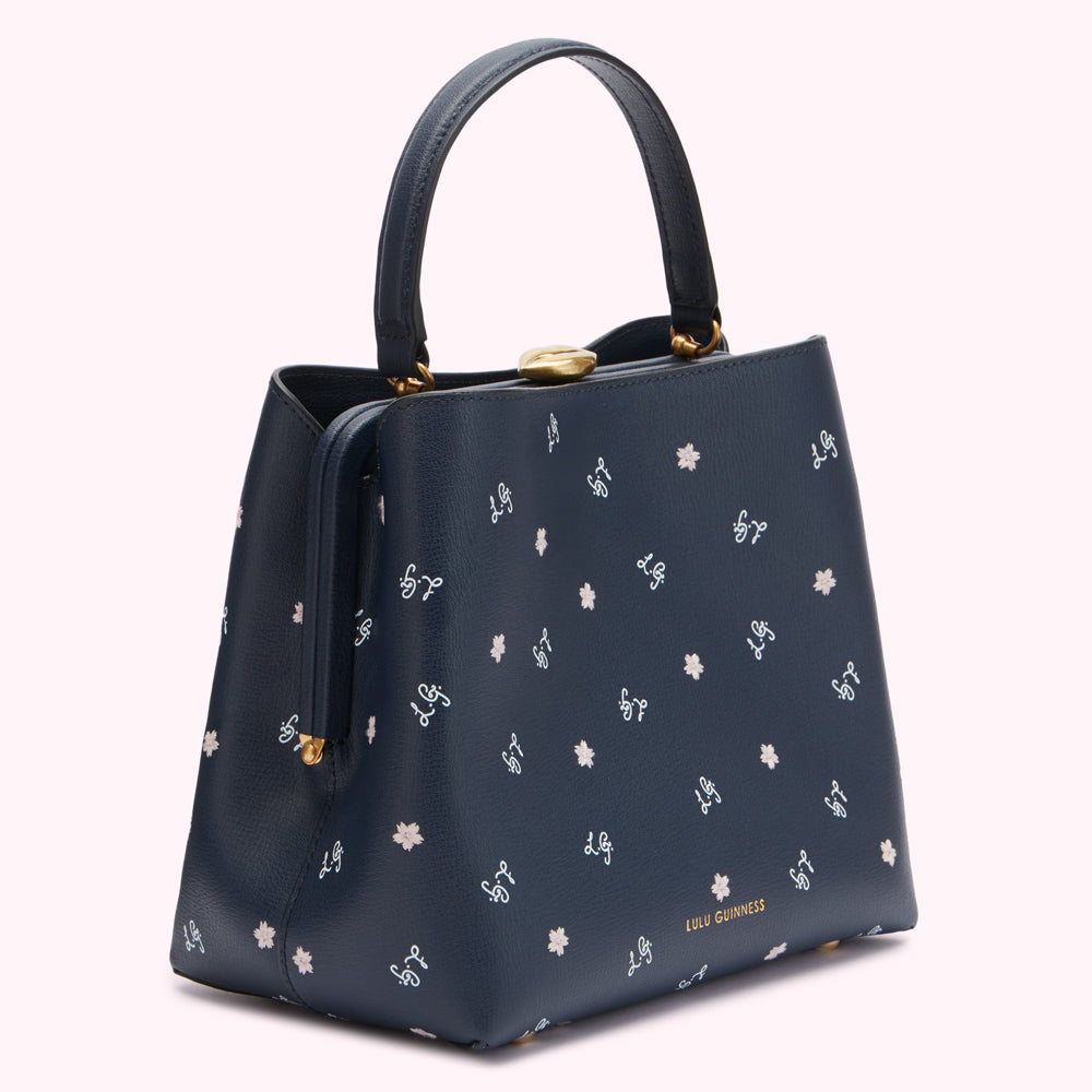 Navy blue Lulu Guinness satchel with a repeating pattern of pale blue stylized flowers and the Lulu Guinness logo.