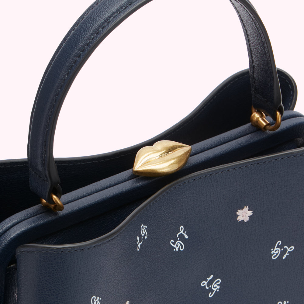 Close-up of a navy blue leather handbag with a gold lip-shaped clasp and white embroidered details.