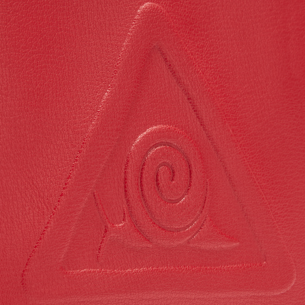 Close-up of a red textured surface with an embossed triangular symbol containing a spiral design.
