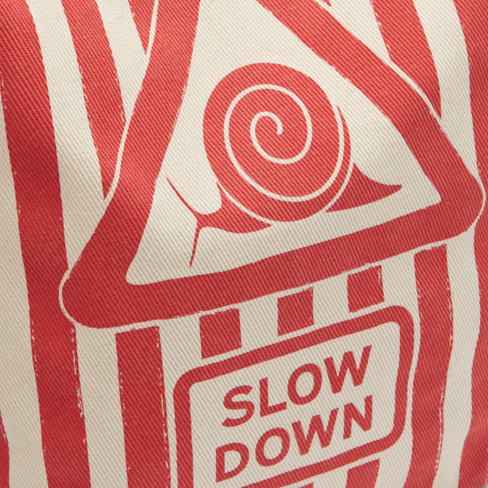 Close-up of beige fabric with a red and white striped pattern and a red triangular sign featuring a snail and the words "SLOW DOWN".