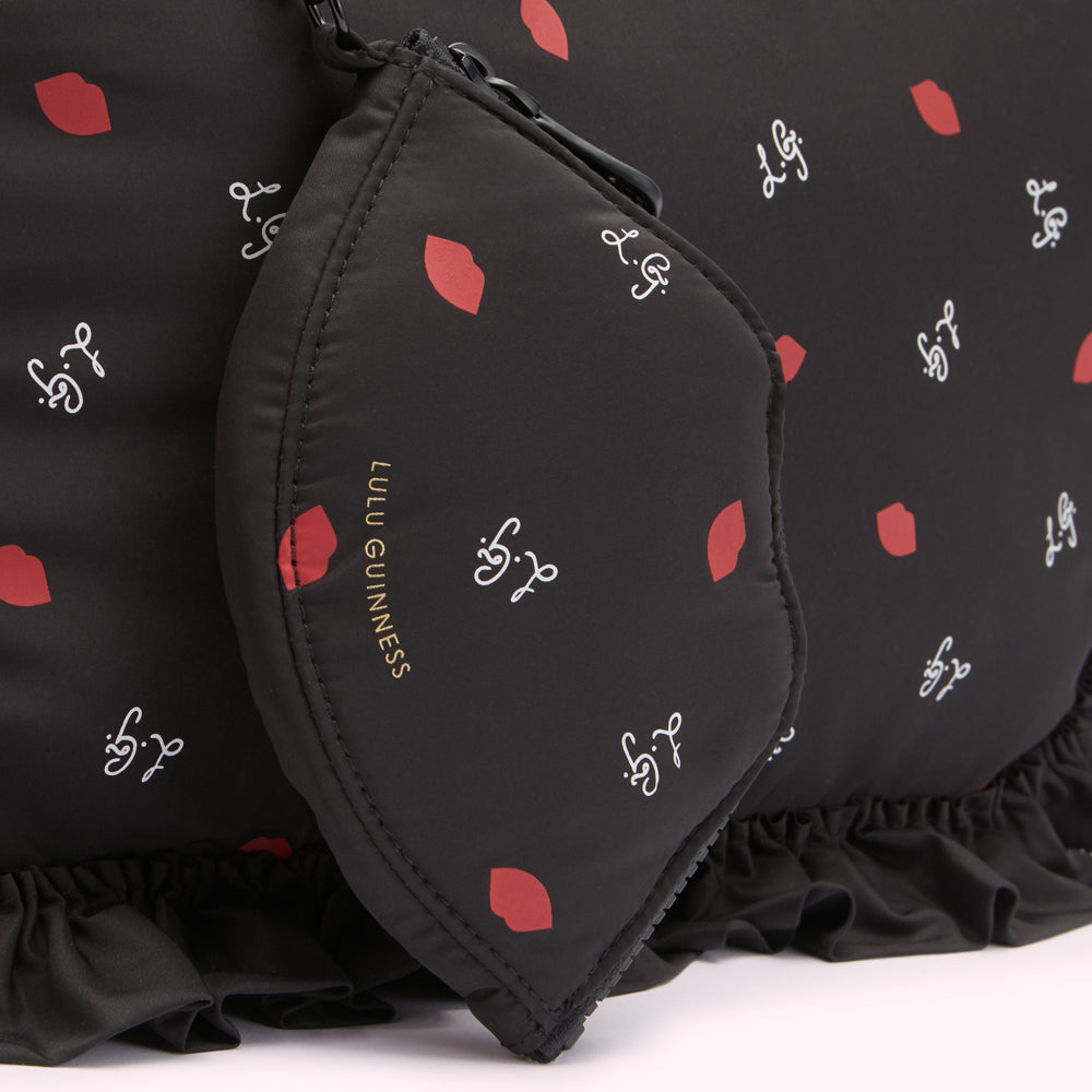 Close-up of a black Lulu Guinness bag and matching pouch featuring a red lips and cursive logo print.
