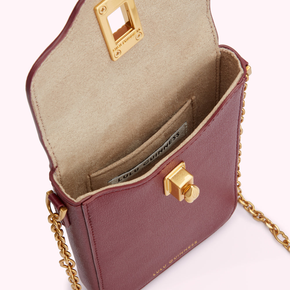 Burgundy Lulu Guinness crossbody bag with gold hardware, open to reveal beige interior and small interior pocket.
