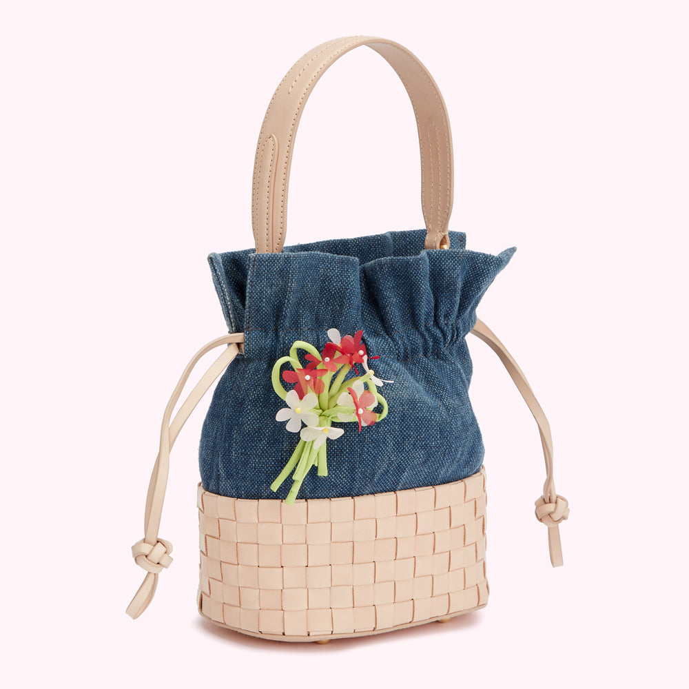 Small denim bucket bag with woven leather bottom and floral embellishment.
