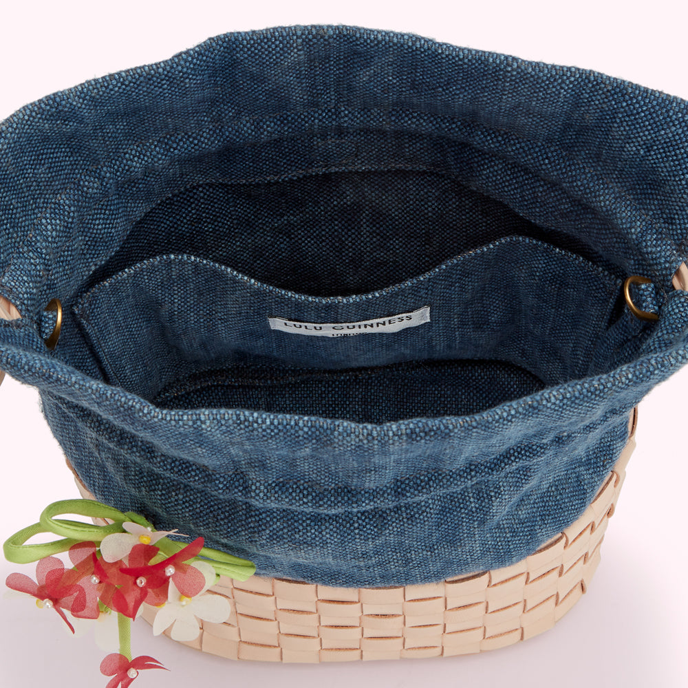 A blue denim Lulu Guinness bucket bag with a tan leather base and a floral embellishment. The bag is open, showing its interior lining.

