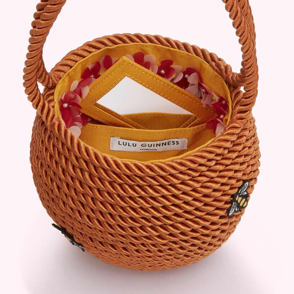 Orange Lulu Guinness rope-textured bucket bag with a yellow interior, floral details, a small mirror, and bee embroidery.