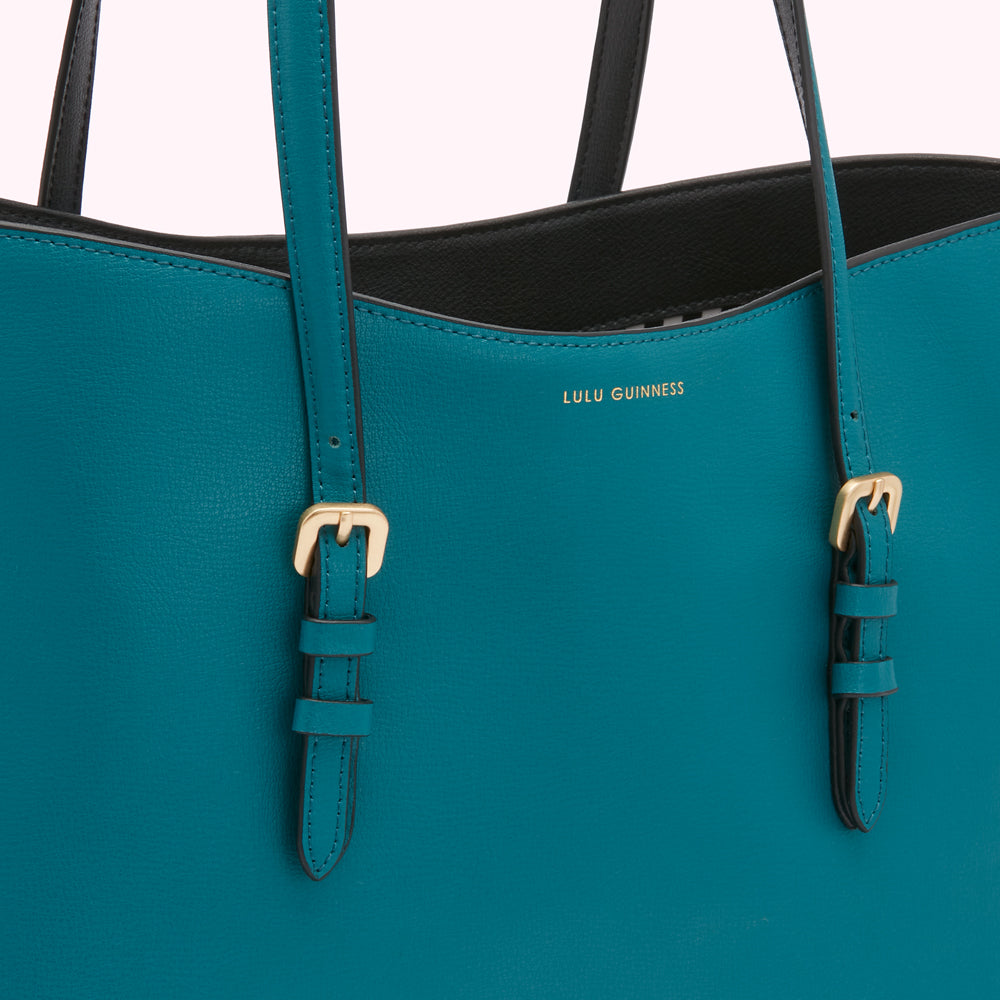 Close-up of a teal Lulu Guinness tote bag with gold buckles.
