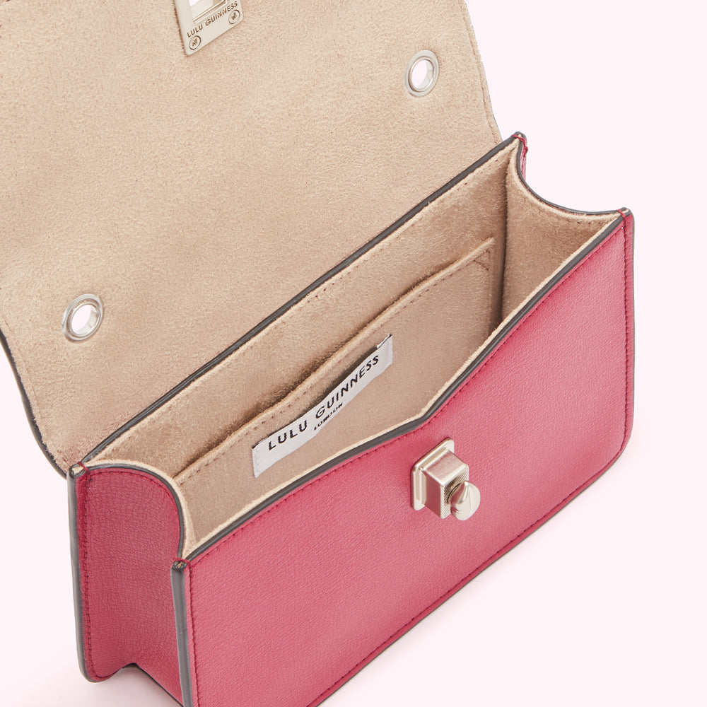 Interior view of a pink Lulu Guinness handbag, showing the beige lining, a small interior pocket, and the brand label.
