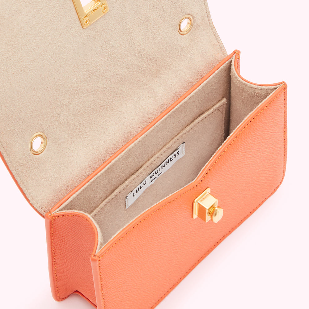 Open coral Lulu Guinness crossbody bag showing beige interior and gold clasp.
