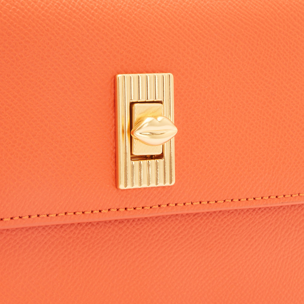 Close-up of an orange textured handbag with a gold lip-shaped clasp.
