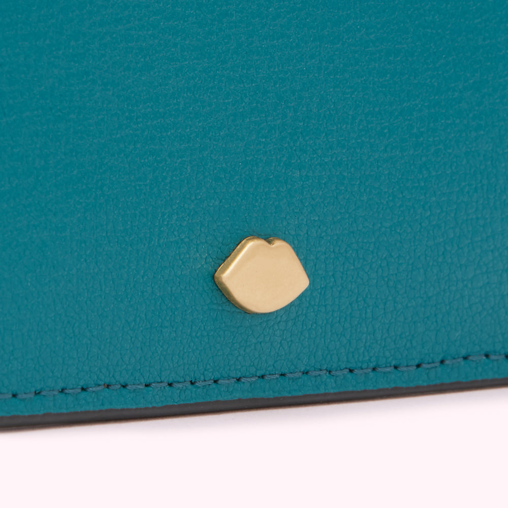 Close-up of a teal leather wallet with a gold lip-shaped detail.
