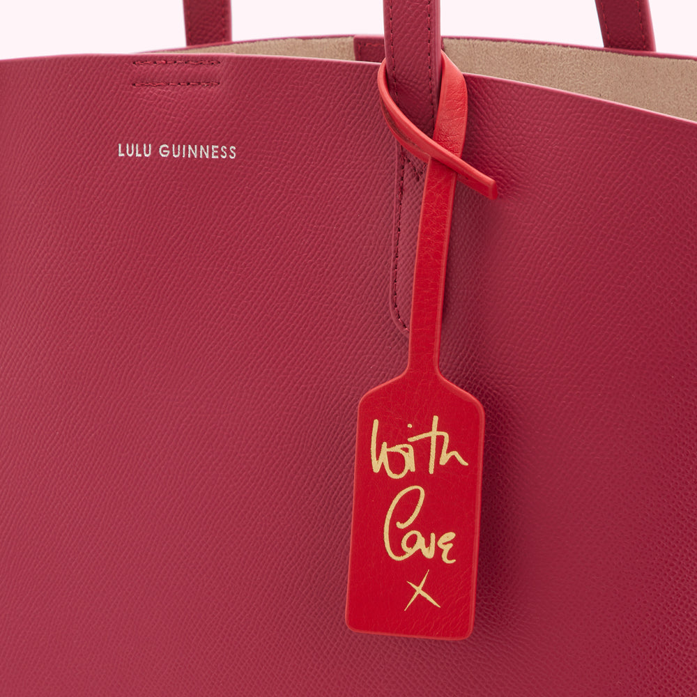 Close-up of a crimson Lulu Guinness tote bag with a red leather tag that says "With Love X" in gold lettering.
