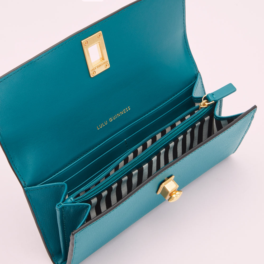 Open teal Lulu Guinness wallet with gold hardware and black and white striped interior.
