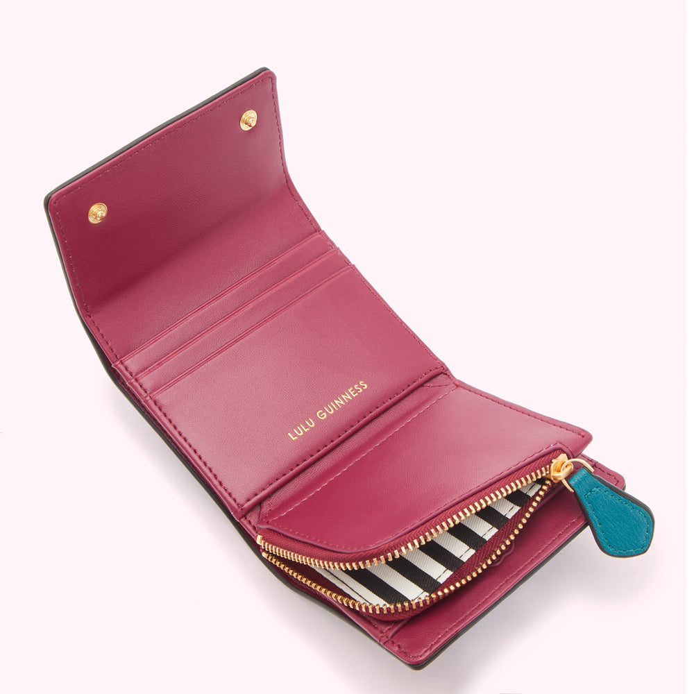 Open crimson Lulu Guinness wallet with black and white striped zipper and teal zipper pull.