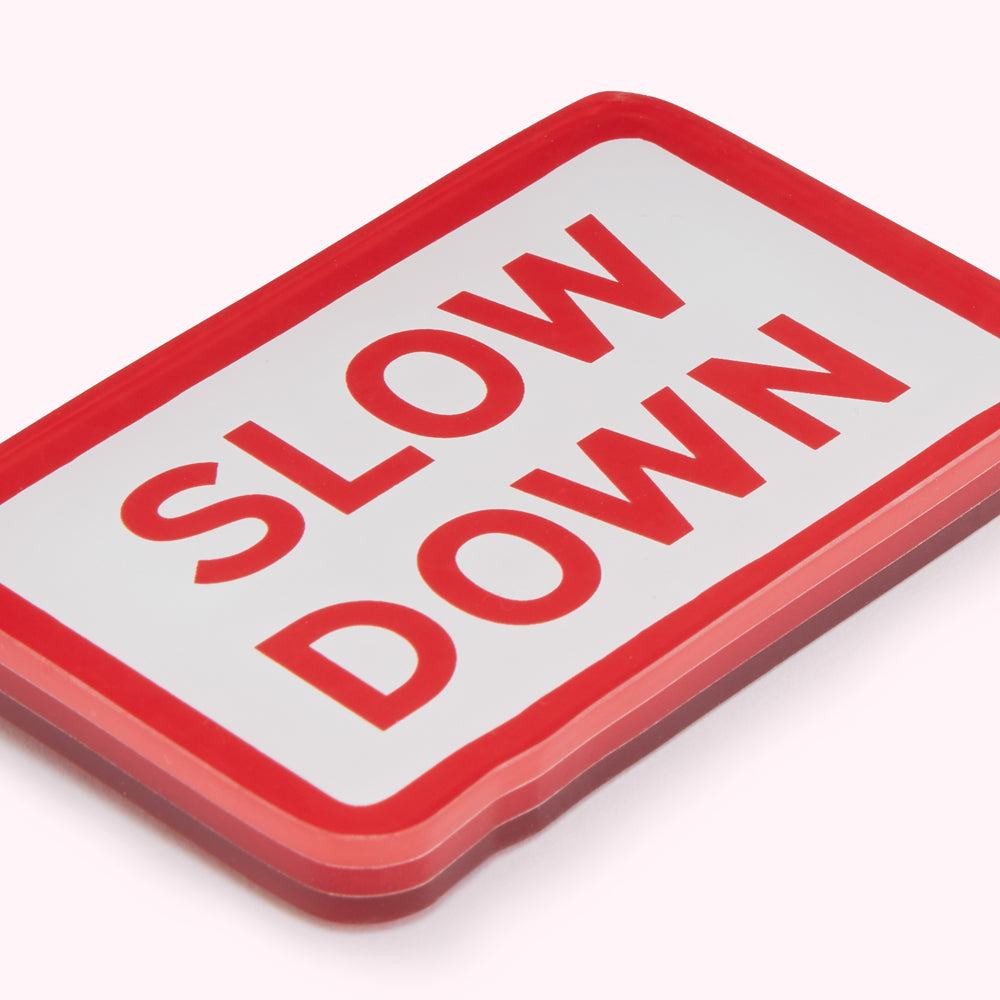 Red and white rectangular sign that says SLOW DOWN in red letters.

