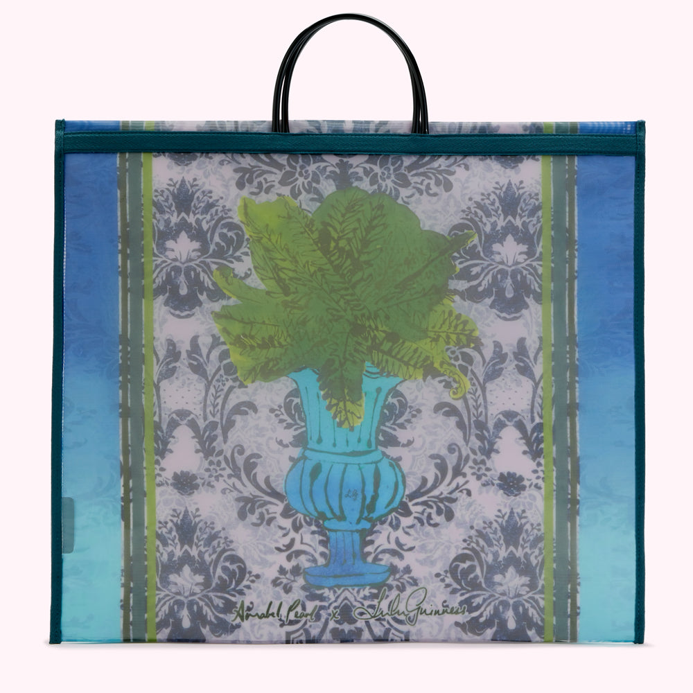 Large teal tote bag with a design featuring a blue urn filled with green ferns against a damask pattern background. The bag has black handles and the designers' signatures are visible at the bottom.