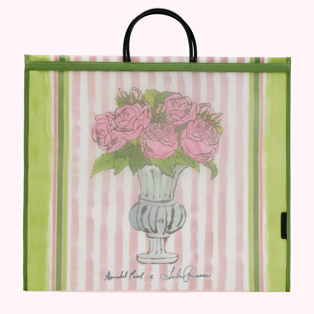 Large reusable tote bag with pink and green striped background, featuring a drawing of pink roses in a light green urn. The bag has green trim and black handles. The artist's names, "Annabel Pearl x Lulu Guinness," are printed on the bag.

