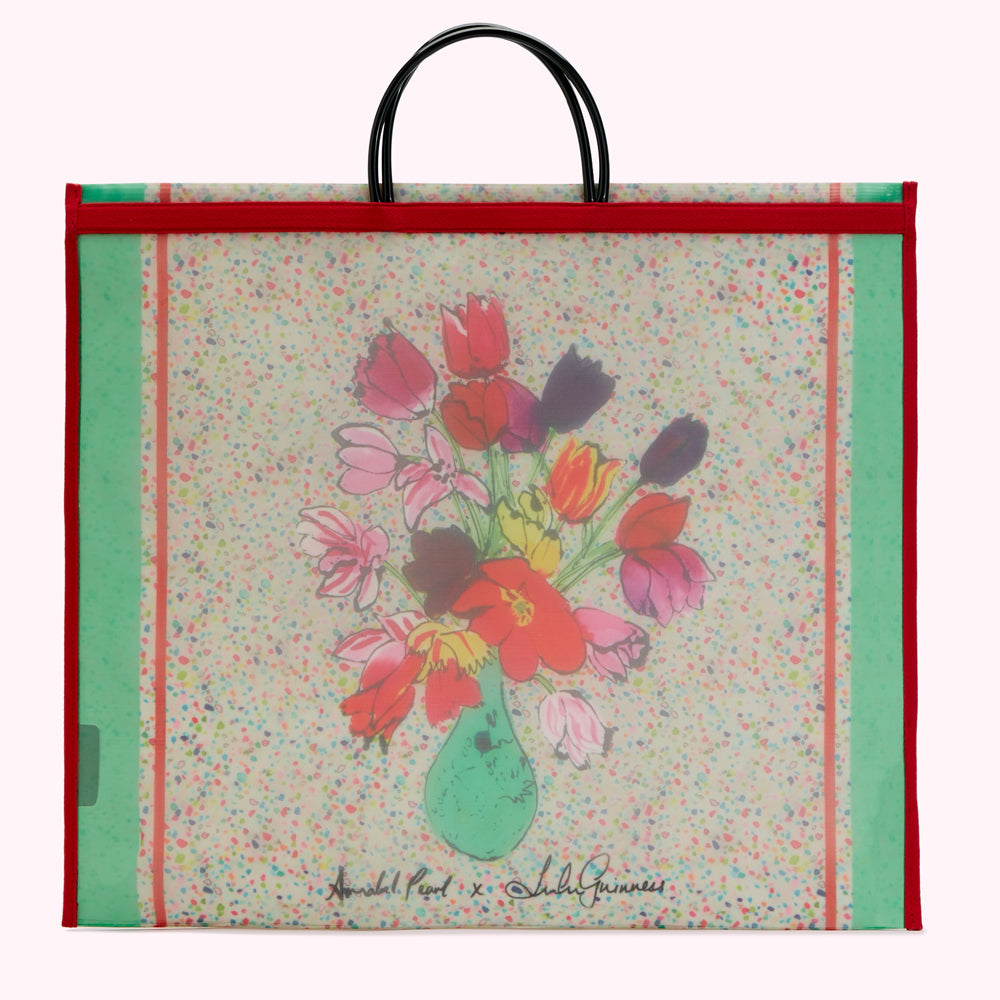 Large red and green tote bag featuring a whimsical illustration of tulips in a vase by Annabel Pearl in collaboration with Lulu Guinness, on an off-white background with multicolored confetti.