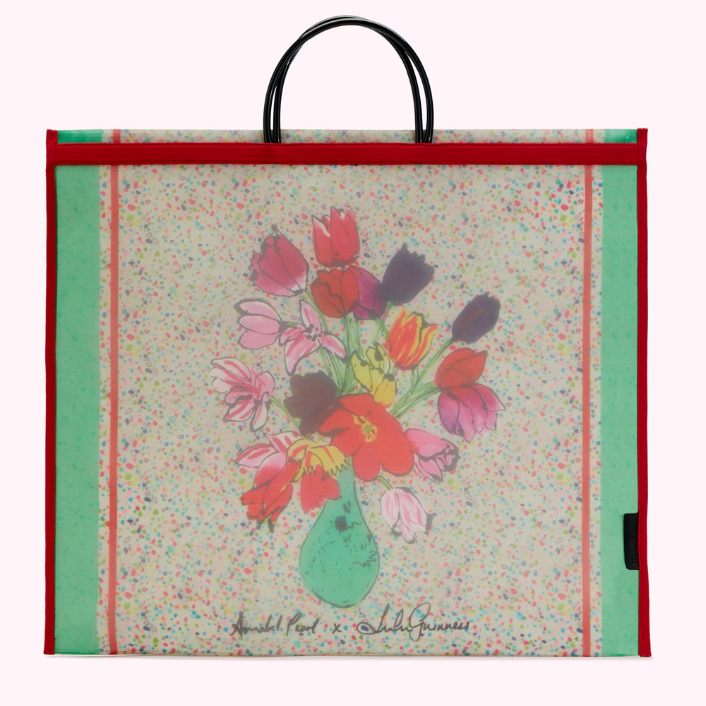 Large tote bag featuring a colorful floral illustration by Annabel Pearl with a cream background speckled with colorful dots and red and green borders; the artist's signature and the name "Lubly Guinness" are displayed in the bottom center.