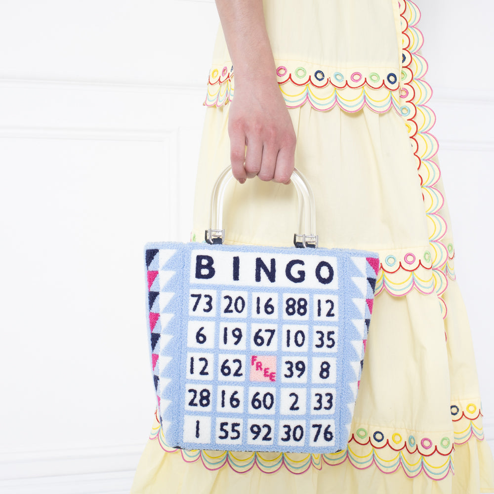 A woman in a yellow dress holds a light blue handbag with a bingo card design.