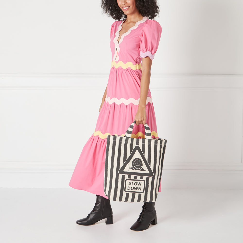 Woman in pink dress holding a black and white tote bag with a snail graphic and the words "Slow Down."
