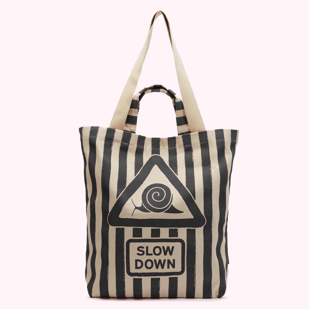 Beige and black striped tote bag with a graphic of a snail in a triangular warning sign that says "SLOW DOWN".
