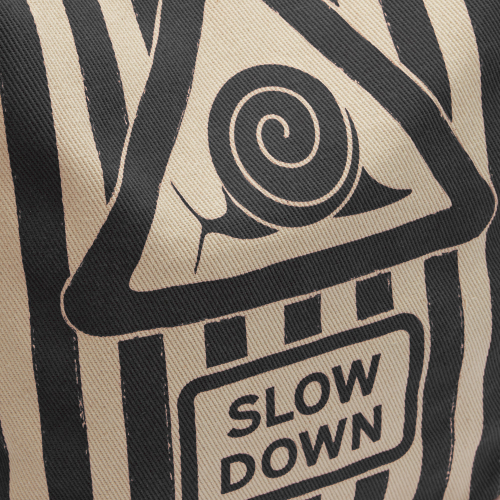 Beige fabric with a black and white graphic of a snail inside a triangular warning sign that says "SLOW DOWN".