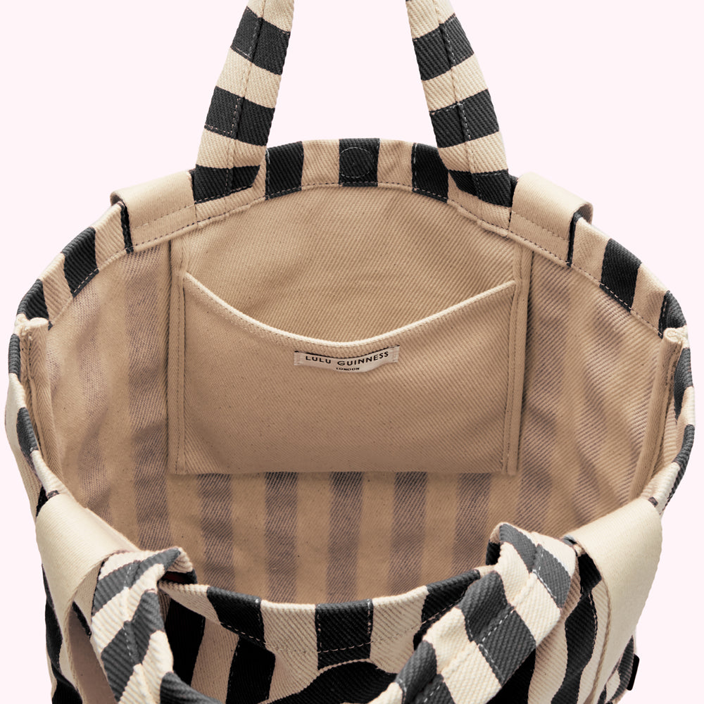 Inside of a beige and black striped tote bag showing a small beige interior pocket with a Lulu Guinness London label.
