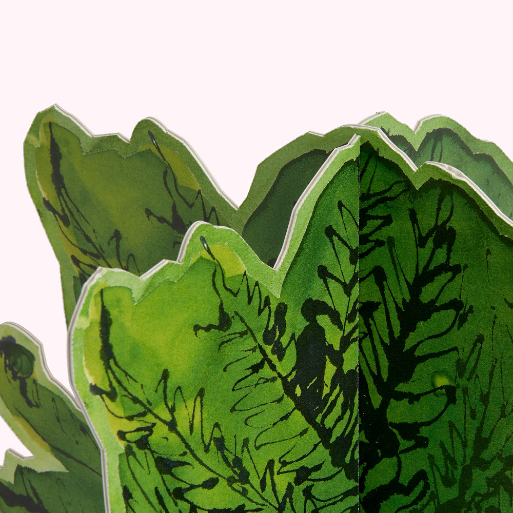 Close-up of a green, leafy, folded paper cutout against a white background.
