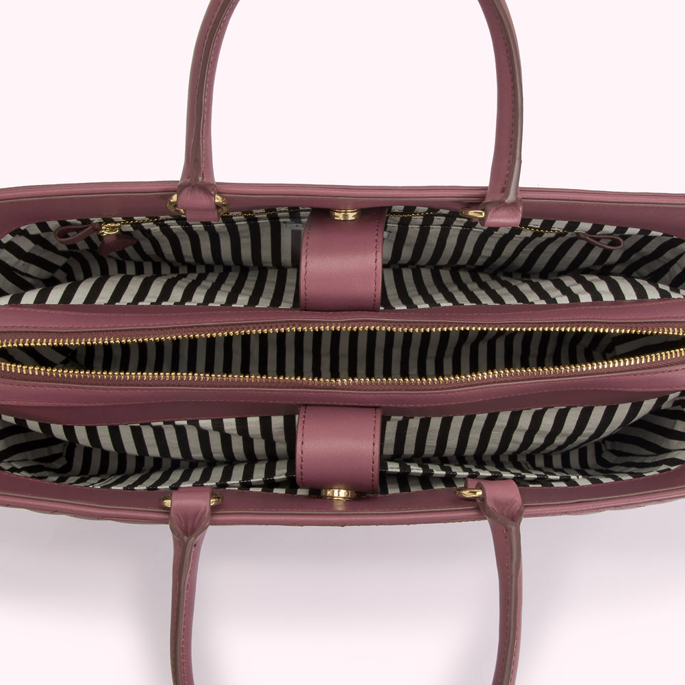 Overhead view of a mauve tote bag with a black and white striped interior and gold zippers.
