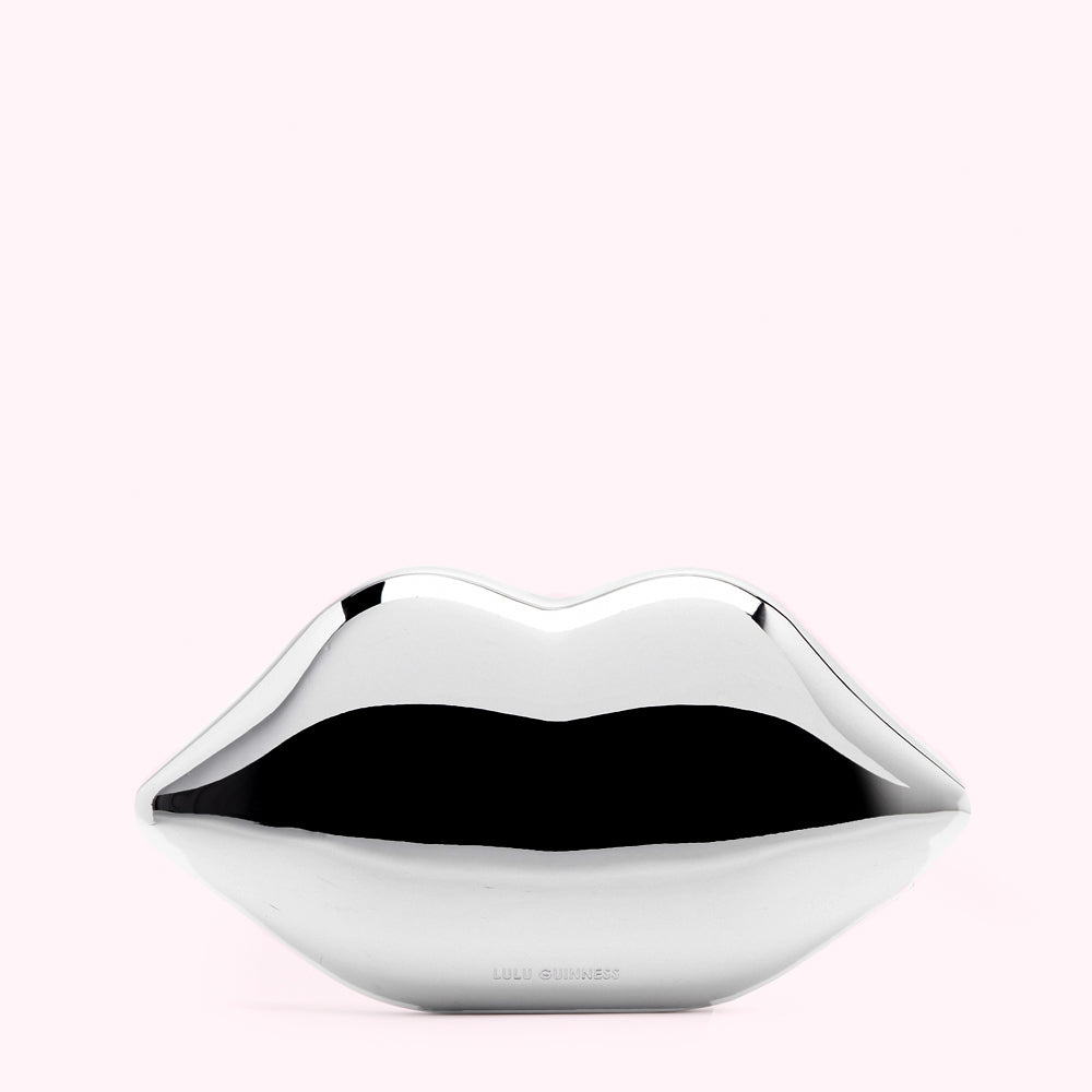 Silver lips clutch bag by Lulu Guinness against a light pink background.
