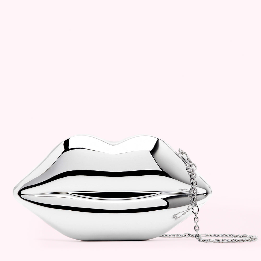 Silver lip-shaped clutch with a silver chain strap against a pink background.
