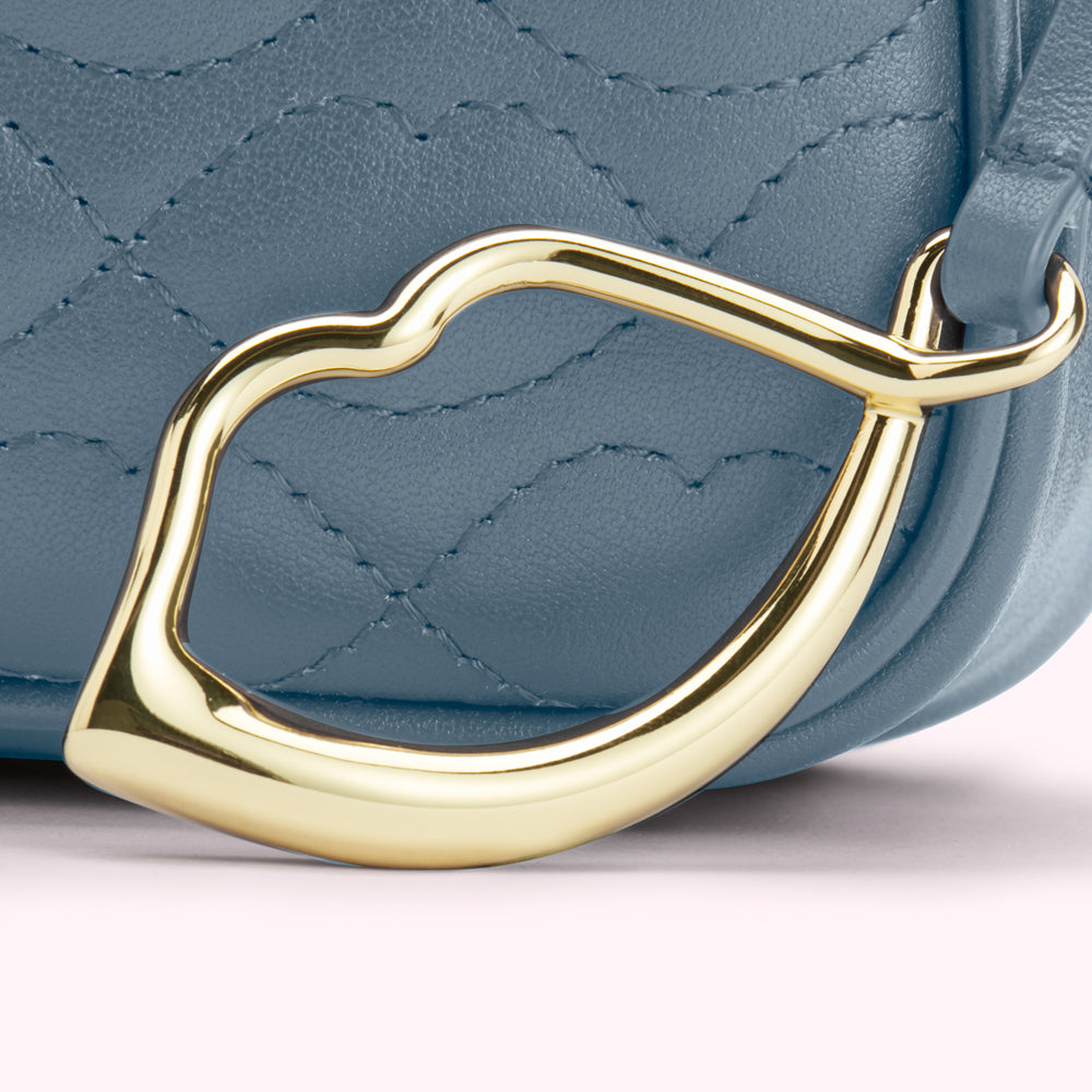 Close-up of a powder blue quilted leather handbag with a gold lip-shaped clasp.
