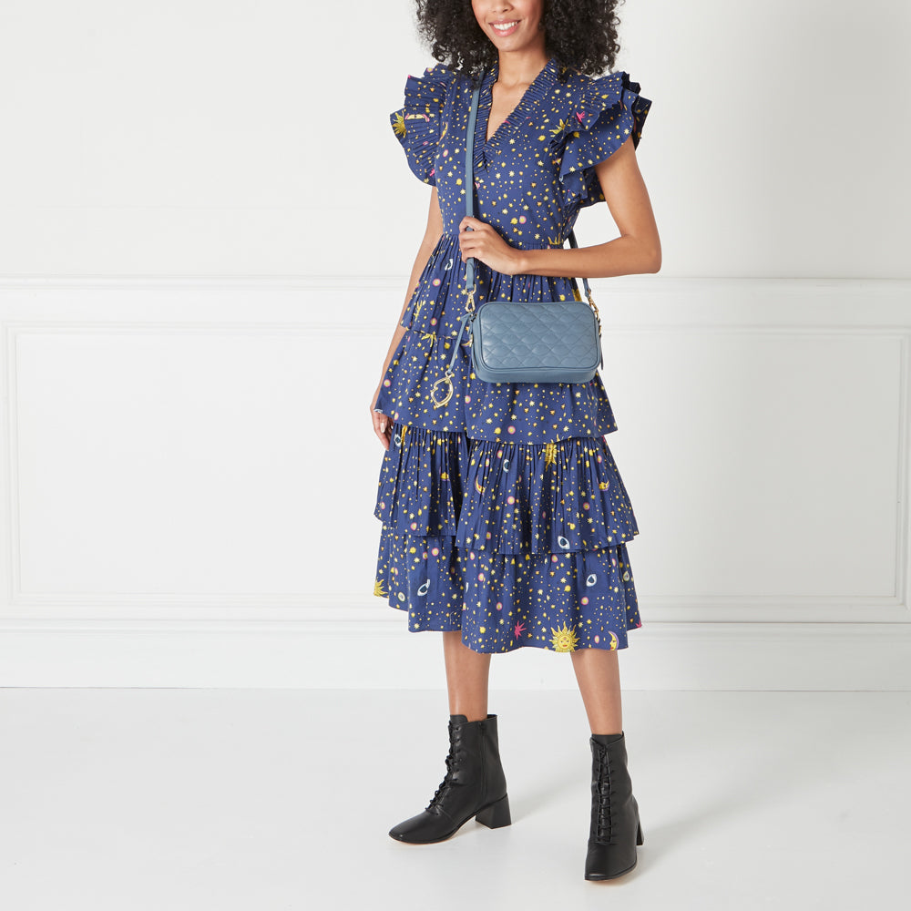 Woman in a blue dress and black boots carrying a blue quilted crossbody bag.
