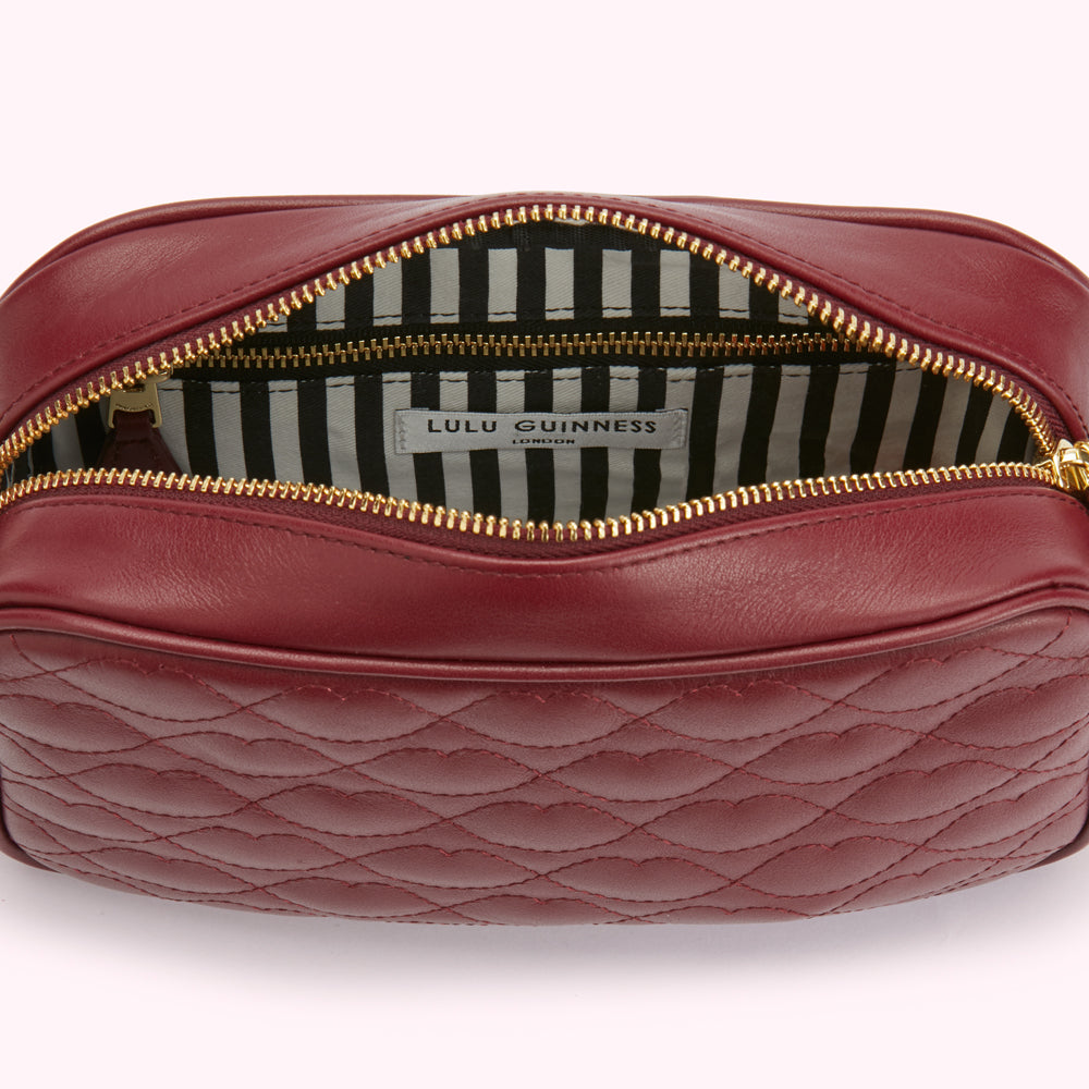 Open dark red quilted leather Lulu Guinness crossbody bag with gold zipper and black and white striped interior.
